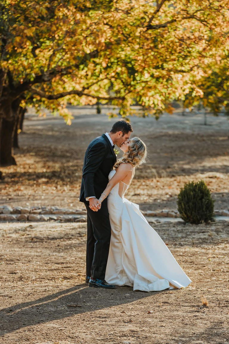 bride and groom kiss in front of autumn trees in Napa