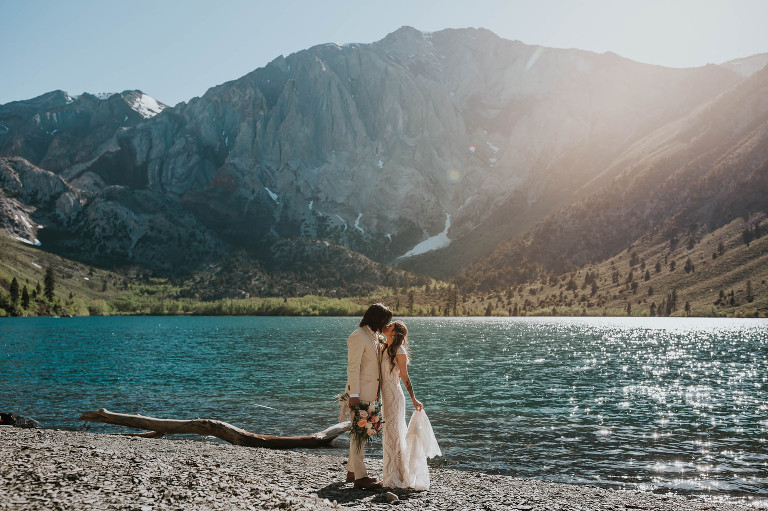 bride and groom hold each other in front of bright blue convict lake