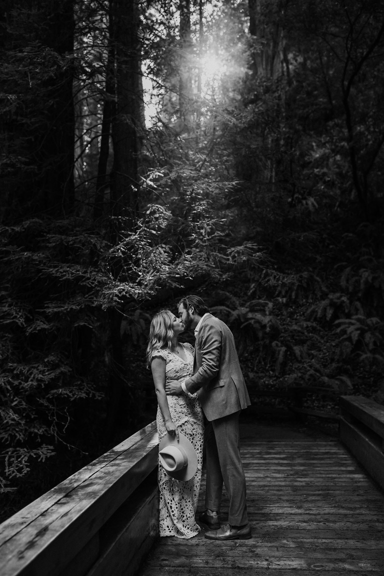 couple kissing as the sun peeks trough the redwood trees in muir woods