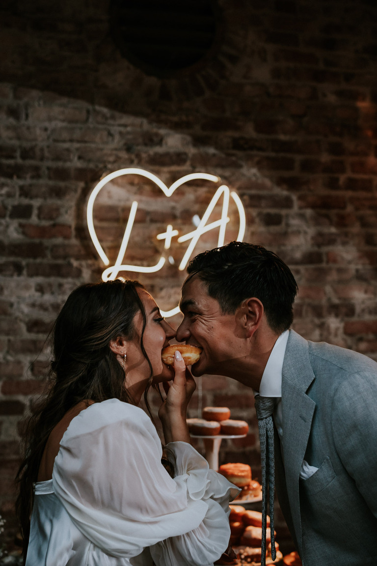 bride and groom each bite into a donut
